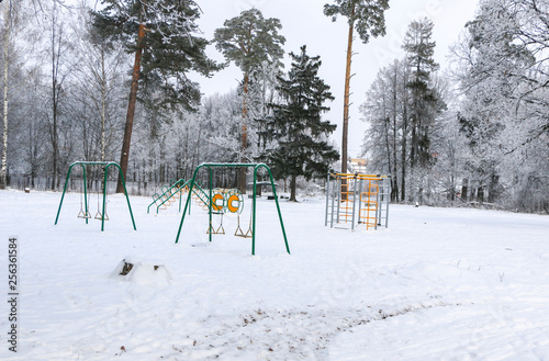 playground with swings, benches, slide and sports units in snow.