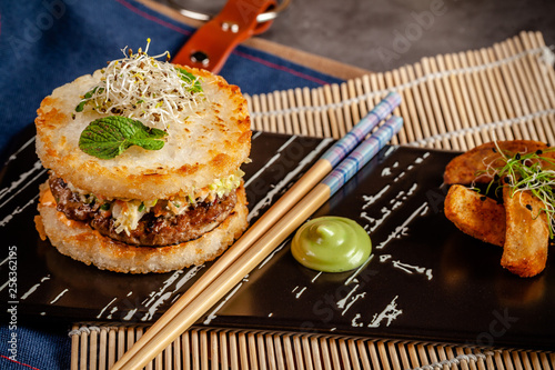 Pan-Asian cuisine concept. Japanese sushi burger made from rice bread, chicken and pork meat patties, lettuce and wasabi sauce. Serving dishes with french fries. copy space photo