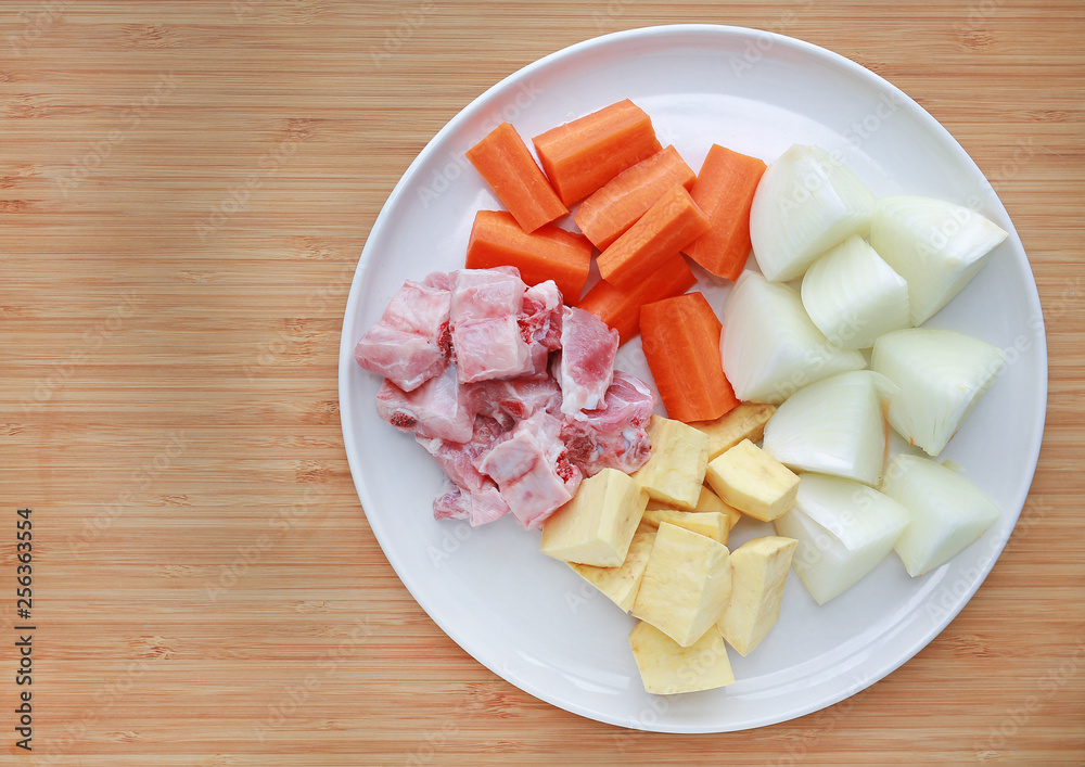 Sliced carrot, onion, pork bone and potato on white plate against wooden background Ingredients for boiling soup. Sliced carrot, onion, pork bone and potato on white plate against wooden background Ingredients for boiling soup.