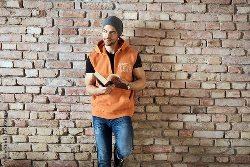 Young man in cap standing at wall reading book