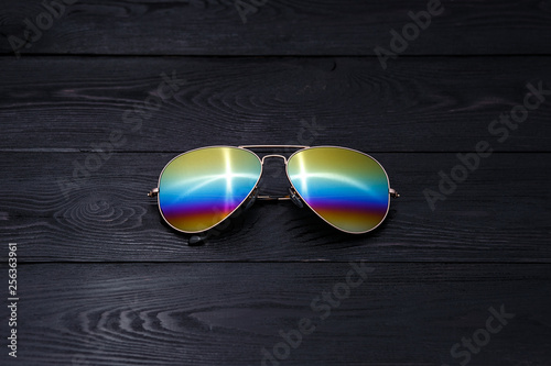 aviators sunglasses with mirrored color lenses made of glass in a gold metal frame covered with gold matte dusting on a black wooden background