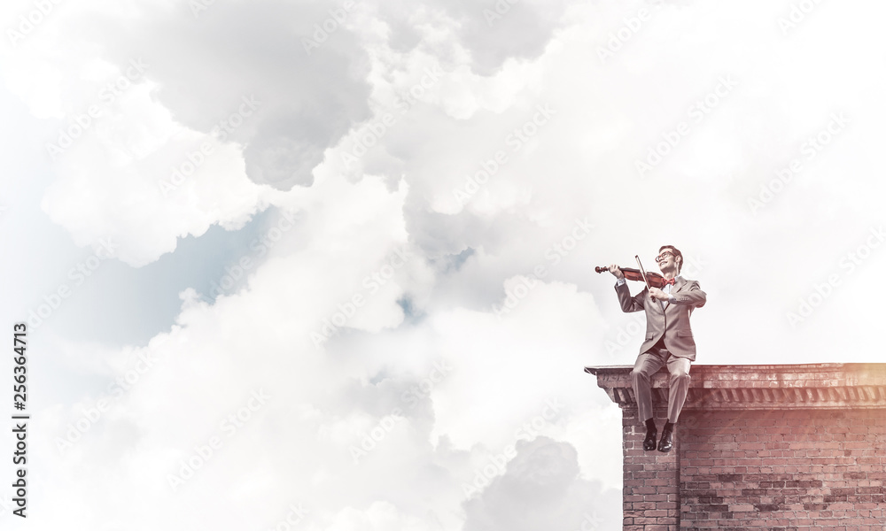 Handsome violinist in glasses on building edge play his melody