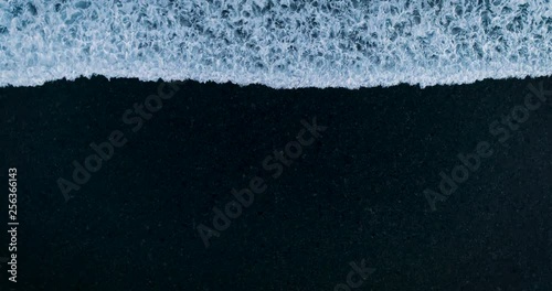 Aerial bird's eye view white foam wave gradually dissolves and disappears on the black sand. Сoncept looped background of disappearance, dissolution 4K