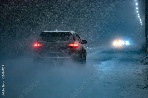 The car goes on the road in an unexpected spring snowfall in the evening.