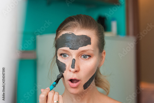 White young woman wearing a face mask at home on a turquoise background. European woman in black mask for the face close up and copy space.