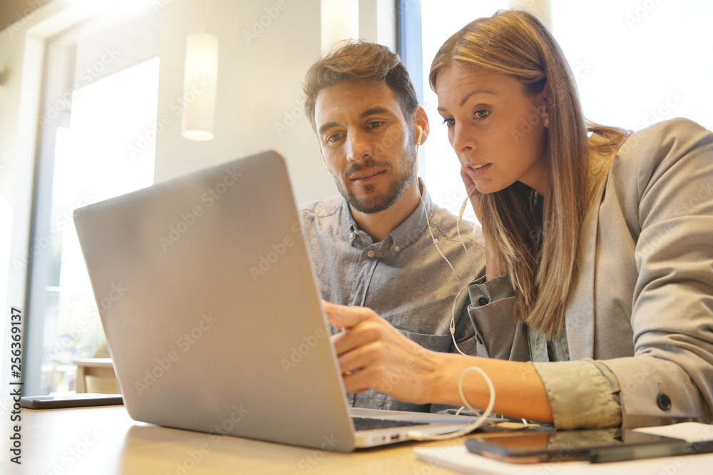 Work colleagues sharing headphones looking at computer