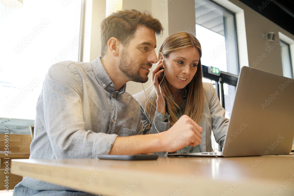 Obraz premium Work colleagues sharing headphones looking at computer