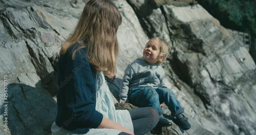 Young mother and her toddler sitting on the rocks by the coast Young mother and her toddler sitting on the rocks by the coast