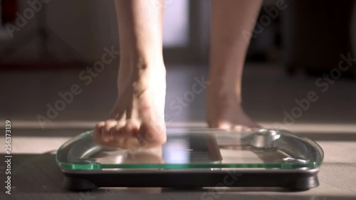 Woman measuring her weight using scales on wooden floor. Healthy diet. photo
