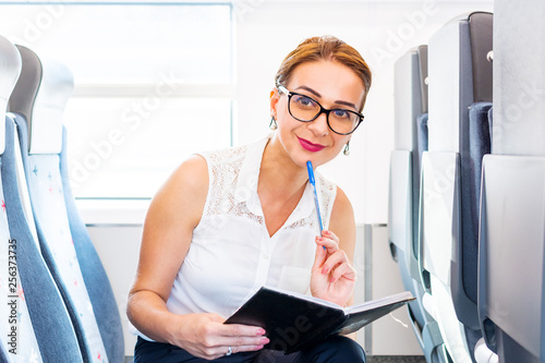 beautiful young woman with notebook and pen smiling while traveling in train