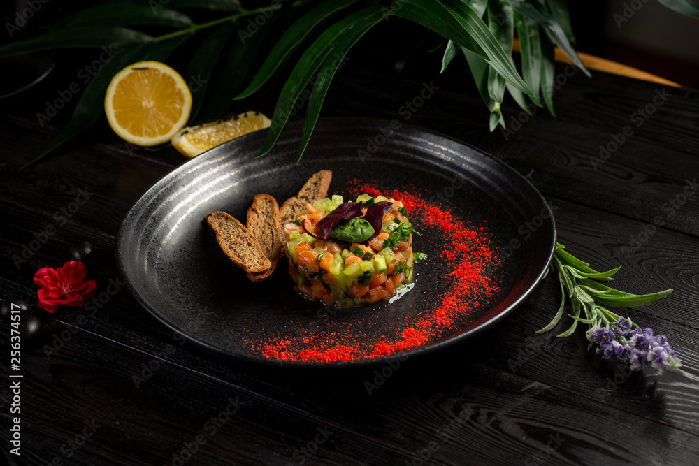salmon tar-tar on a black plate on a wooden background