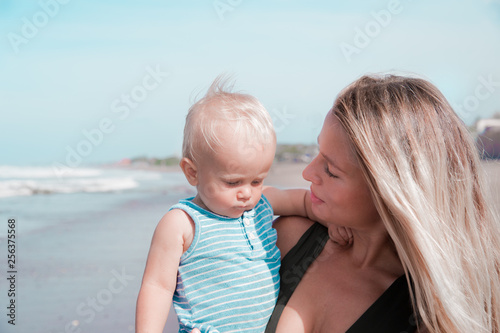 Young millennial mother is spending time with her cute baby boy on the beach.