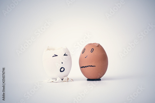 Two broken eggs in the form of human head (white and black)  complain to each other. Concept.