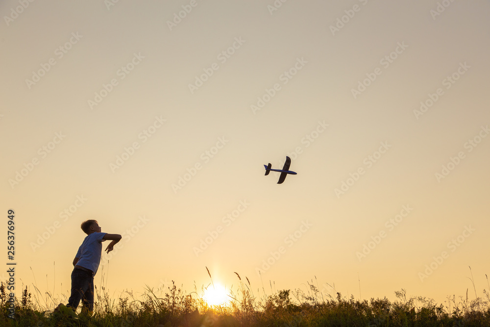 Young happy kid playing toy plane outside on summer sunset grassy hill. Horizontal color photography.