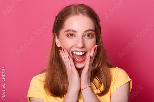 Happy young adorable female screms something in triumph, has wonderful news, dressed in casual yellow outfit, wants to share her happiness, poses in photo studio. People and achievement concept.