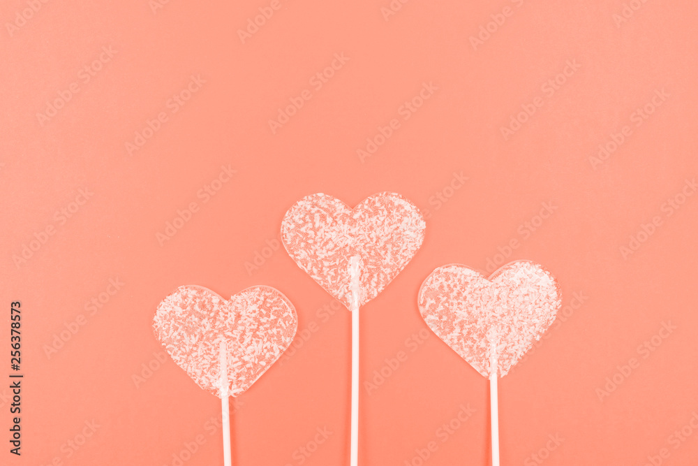 Lollipops in the shape of hearts on a coral background. Top view. Flat lay with copy space.