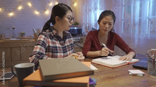 Two angry female students arguing doing homework at home. group of college girls having bad teamwork shouting screaming each other with textbook. roommate unsatisfied report project in kitchen night.