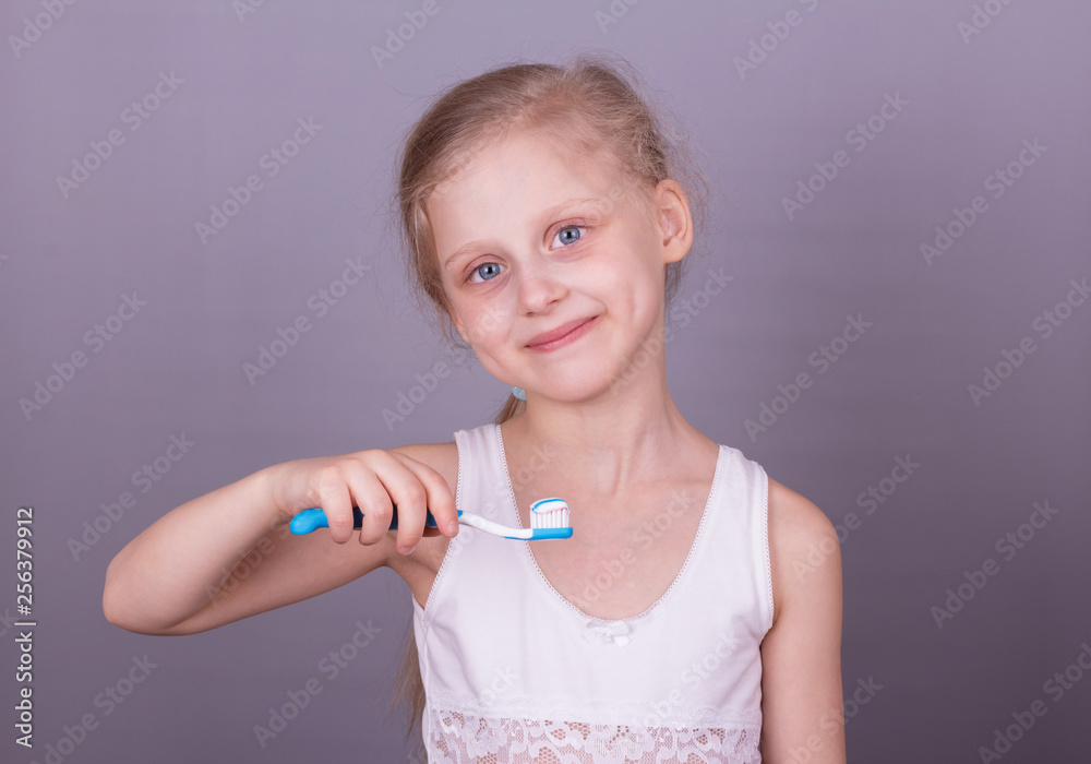?oncept of healthy lifestyle. Caring for children's teeth. Girl brushing her teeth over grey background ?oncept of healthy lifestyle. Caring for children's teeth. Girl brushing her teeth over grey background
