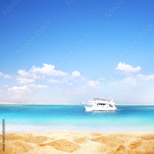 Summer background, nature of tropical golden beach with blue sky and white clouds. Golden sand beach close-up, turquoise water sea, white yacht, landscape. Copy space, summer vacation concept. © Laura Pashkevich