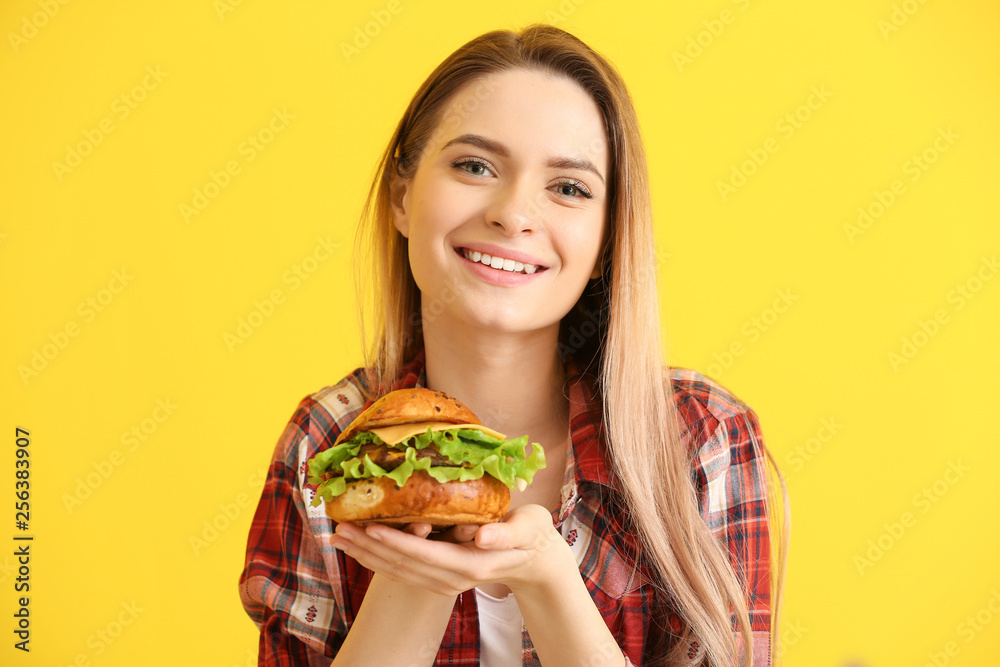 Beautiful young woman with tasty burger on color background