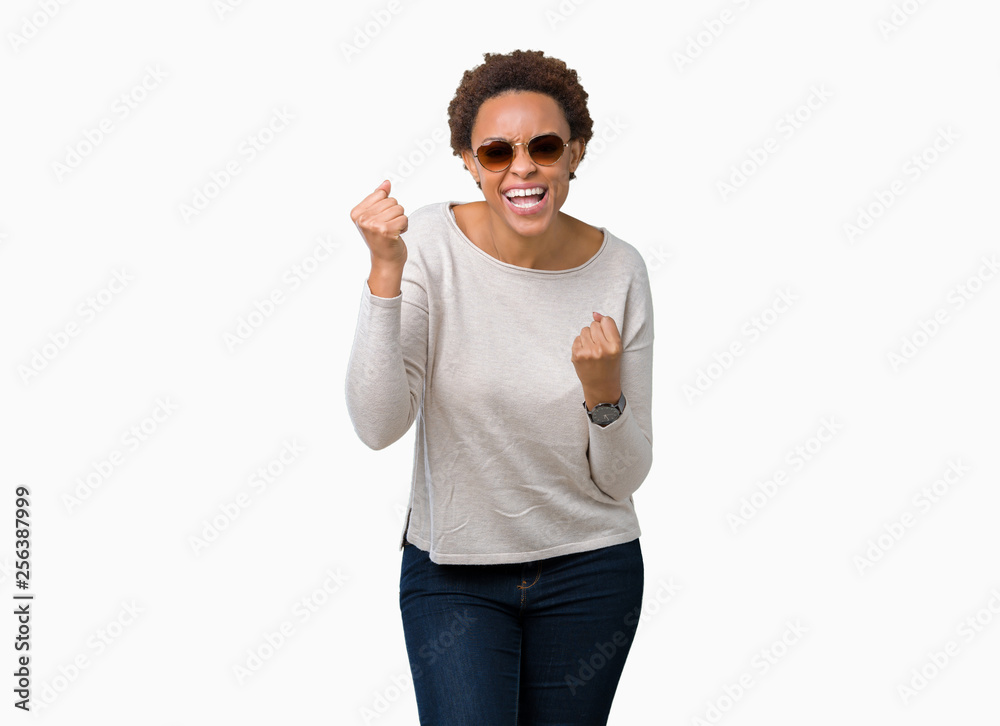 Beautiful young african american woman wearing sunglasses over isolated background very happy and excited doing winner gesture with arms raised, smiling and screaming for success. Celebration concept. Beautiful young african american woman wearing sunglasses over isolated background very happy and excited doing winner gesture with arms raised, smiling and screaming for success. Celebration concept.