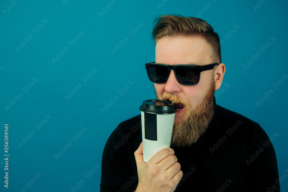 young fashionable handsome guy in a black turtleneck, holding a white plastic Cup of coffee on a blue background, a man drinking coffee young fashionable handsome guy in a black turtleneck, holding a white plastic Cup of coffee on a blue background, a man drinking coffee