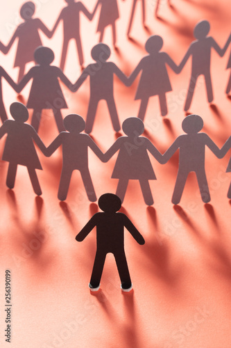 Paper human figure standing in front of paper people holding hands on red surface. Bulling, conflict, segregation concept.