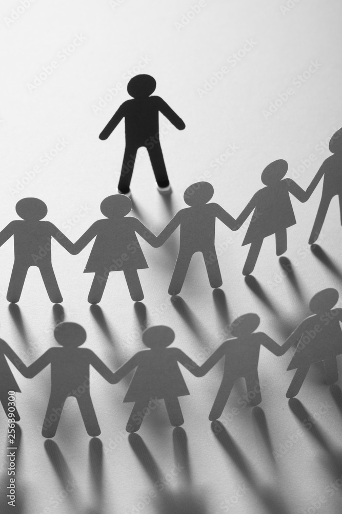 Paper human figure standing in front of paper people holding hands on white surface. Bulling, conflict, minorities concept. Paper human figure standing in front of paper people holding hands on white surface. Bulling, conflict, minorities concept.