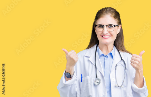 Middle age mature doctor woman wearing medical coat over isolated background success sign doing positive gesture with hand  thumbs up smiling and happy. Looking at the camera with cheerful expression