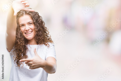 Beautiful brunette curly hair young girl wearing casual t-shirt over isolated background smiling making frame with hands and fingers with happy face. Creativity and photography concept.
