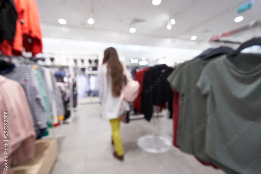 Beautiful blurred background of a women's clothing store in a mall, a young girl walks and chooses clothes. Shopping mall or department store with blurred background and bokeh light.