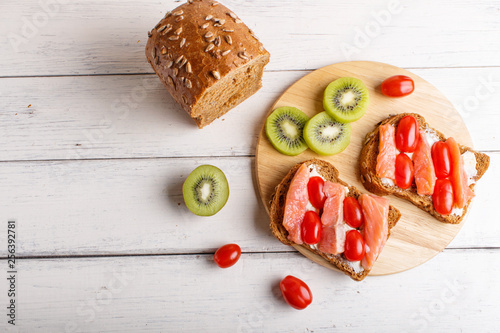 Smoked salmon sandwiches with butter and cherry tomatoes on white wooden background.