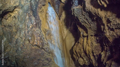 Water is falling from a hole in the wall in a cave. It is falling down into a small lake. photo