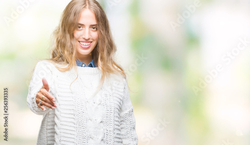 Beautiful young blonde woman wearing winter sweater over isolated background smiling friendly offering handshake as greeting and welcoming. Successful business. © Krakenimages.com