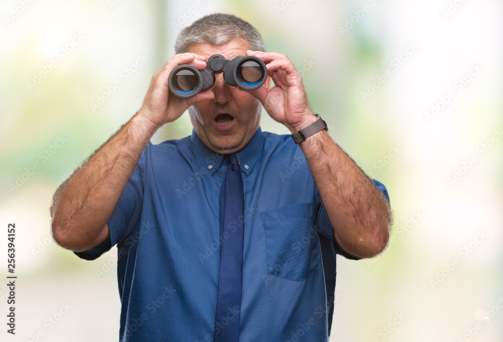 Handsome senior man looking through binoculars over isolated background scared in shock with a surprise face, afraid and excited with fear expression Handsome senior man looking through binoculars over isolated background scared in shock with a surprise face, afraid and excited with fear expression