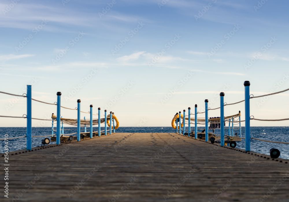 Obraz premium wooden platform with blue posts with ropes and orange lifebuoys on the background of the sea and sky with clouds Egypt Dahab South Sinai