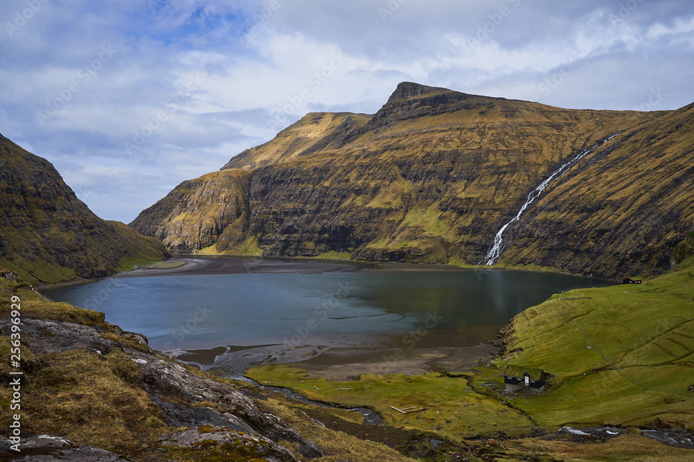 Scenic landscape picture on sea water lagoon or lake between mountains without trees in willage Saksun or danish Saksen in faroese island Streymoy in north atlantic in spring sunny, cloudy morning. 