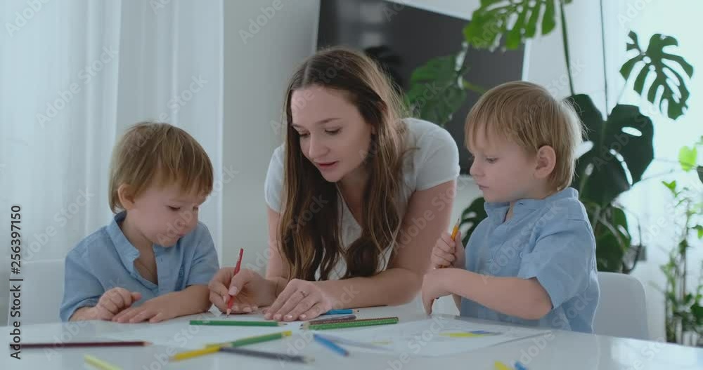 Young Mom and two sons 2-4 years old draw pencils drawing on boomega sitting at the living room table in slow motion Young Mom and two sons 2-4 years old draw pencils drawing on boomega sitting at the living room table in slow motion