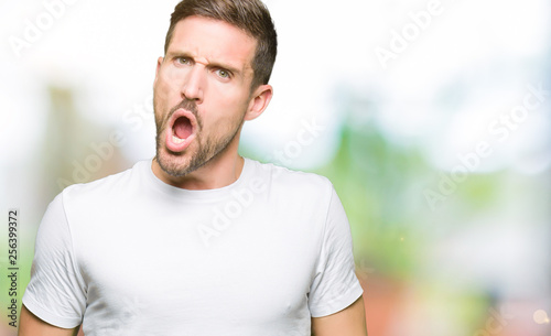 Handsome man wearing casual white t-shirt In shock face, looking skeptical and sarcastic, surprised with open mouth