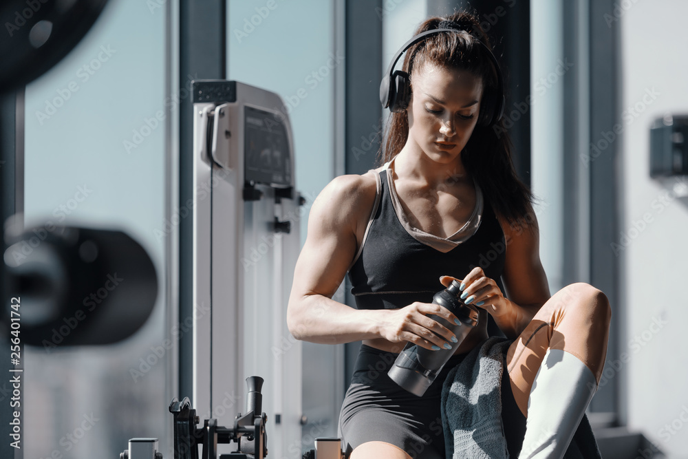 Young Caucasian strong muscular female bodybuilder sitting in gym with  headphones on ears and water in hands. Suffer the pain of discipline of  suffer the pain of regret. Stock-Foto | Adobe Stock
