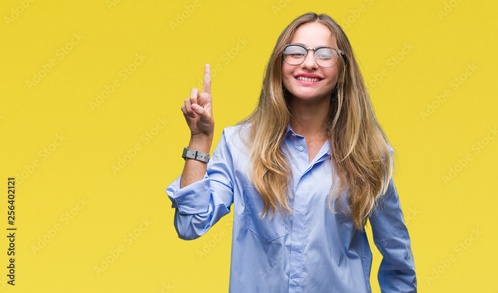 Young beautiful blonde business woman wearing glasses over isolated background showing and pointing up with finger number one while smiling confident and happy. Young beautiful blonde business woman wearing glasses over isolated background showing and pointing up with finger number one while smiling confident and happy.