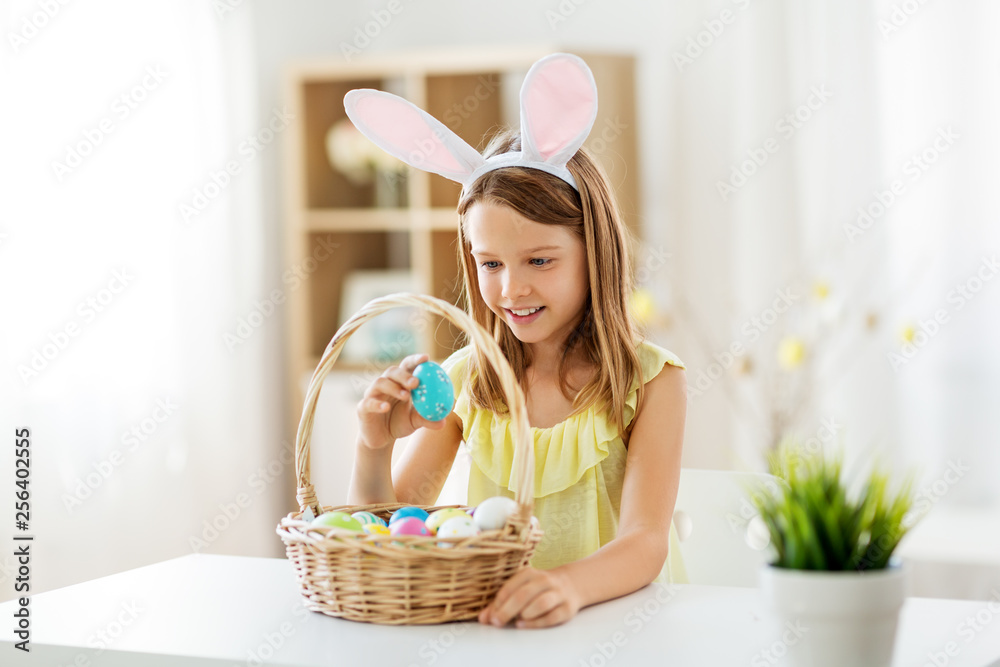 easter, holidays and people concept - happy girl wearing bunny ears headband with basket of colored eggs at home easter, holidays and people concept - happy girl wearing bunny ears headband with basket of colored eggs at home