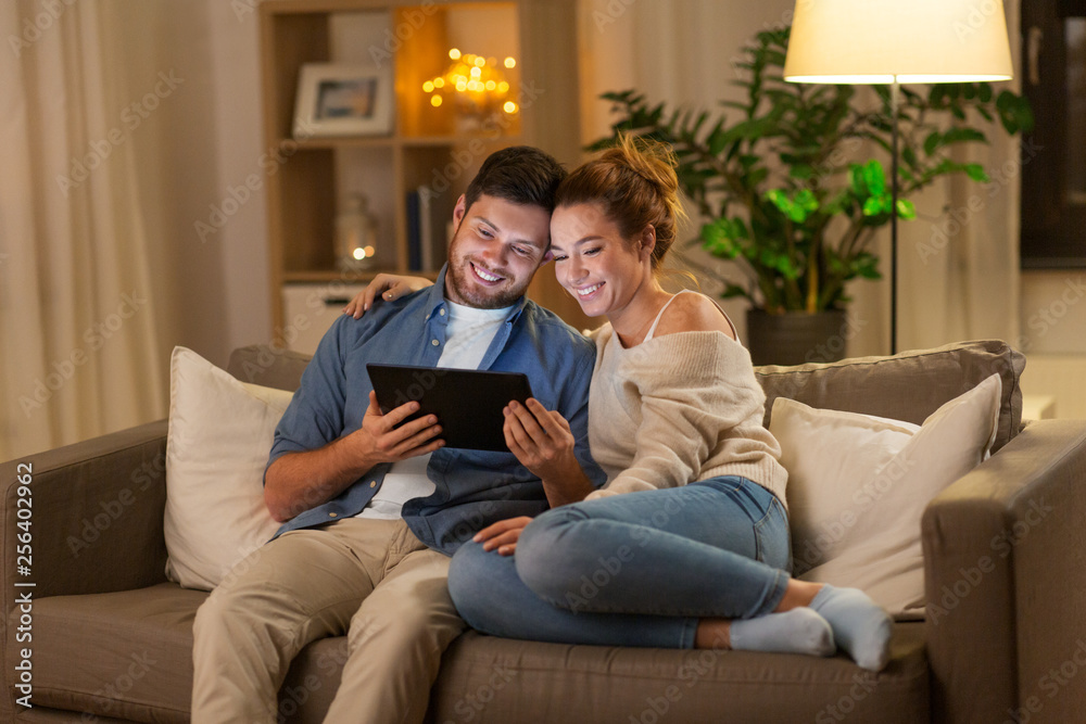 technology, internet and people concept - happy couple using tablet computer at home in evening technology, internet and people concept - happy couple using tablet computer at home in evening