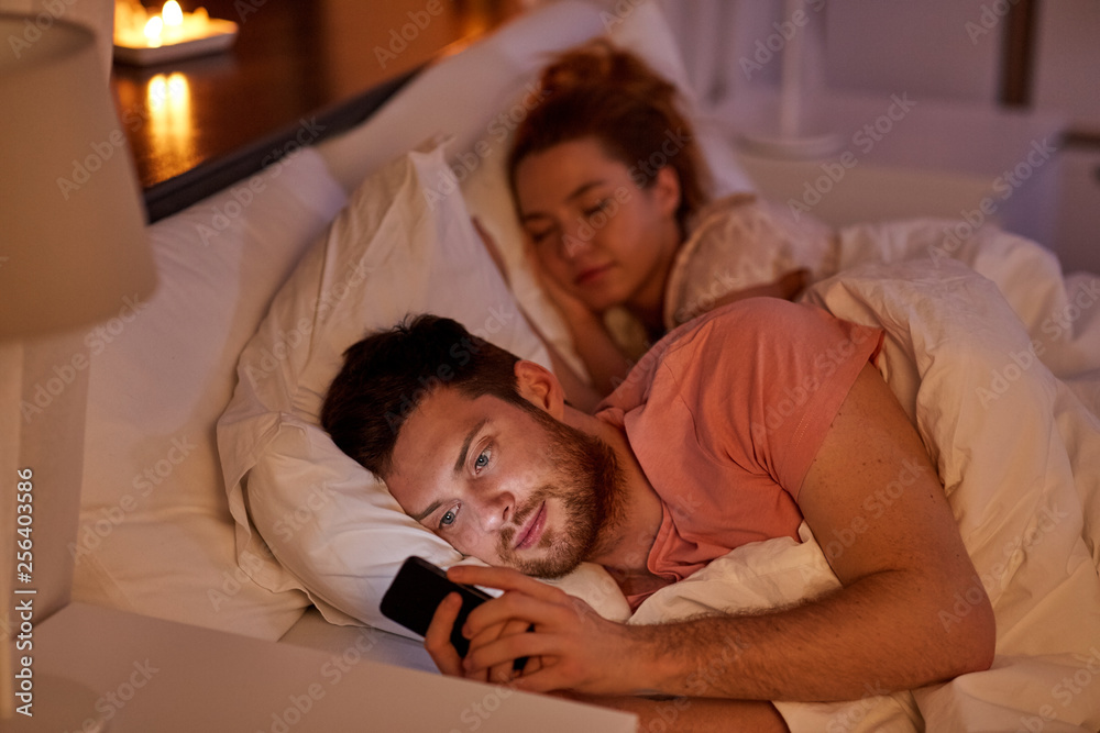 technology, internet addiction and cheat concept - man using smartphone at night while girlfriend is sleeping technology, internet addiction and cheat concept - man using smartphone at night while girlfriend is sleeping