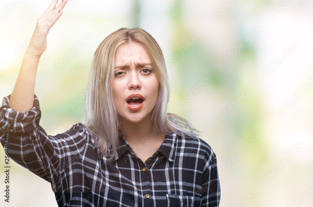 Young blonde woman over isolated background angry and mad raising fist frustrated and furious while shouting with anger. Rage and aggressive concept.