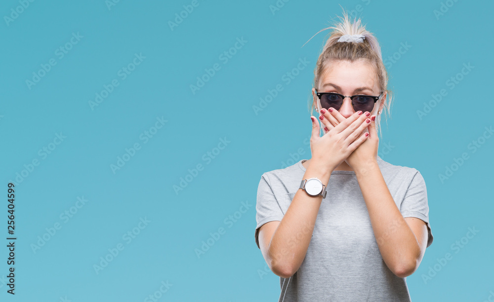 Fototapeta premium Young blonde woman wearing sunglasses over isolated background shocked covering mouth with hands for mistake. Secret concept.