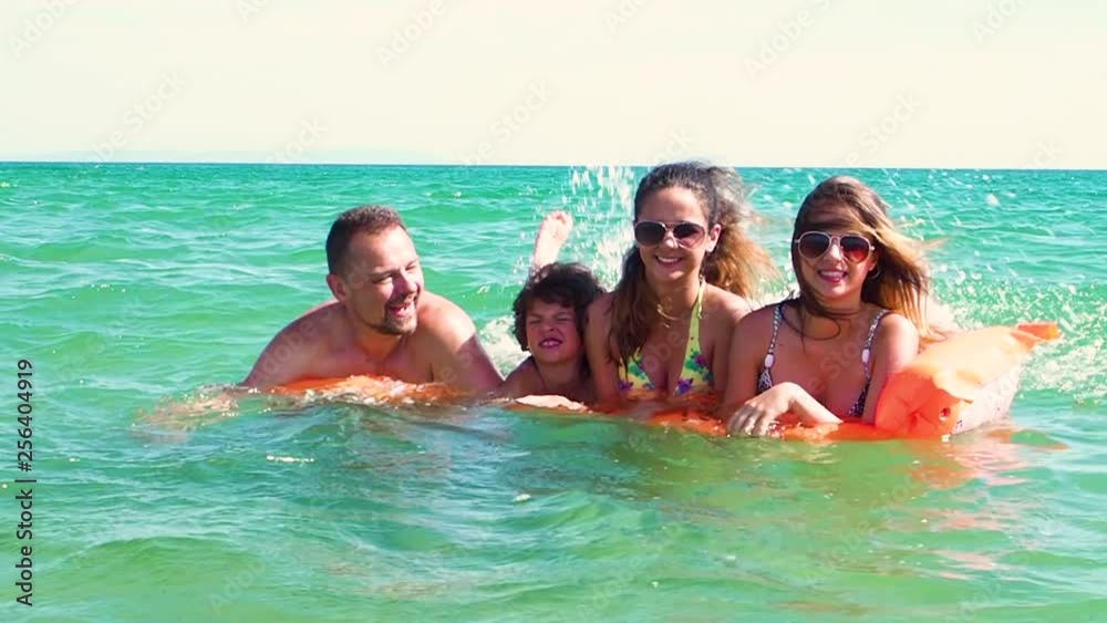 Happy family of four in vacation at sea shore. Happy family with yellow mattress bathes in sea. happy mum daddy and two children play in water. Slow Motion Happy family of four in vacation at sea shore. Happy family with yellow mattress bathes in sea. happy mum daddy and two children play in water. Slow Motion