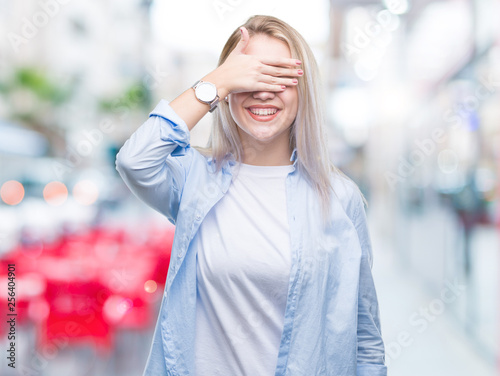 Young blonde woman over isolated background smiling and laughing with hand on face covering eyes for surprise. Blind concept.