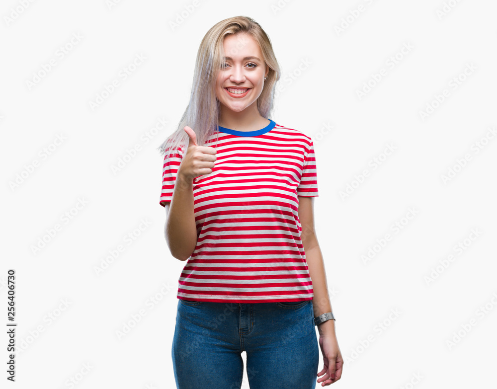 Young blonde woman over isolated background doing happy thumbs up gesture with hand. Approving expression looking at the camera with showing success. Young blonde woman over isolated background doing happy thumbs up gesture with hand. Approving expression looking at the camera with showing success.