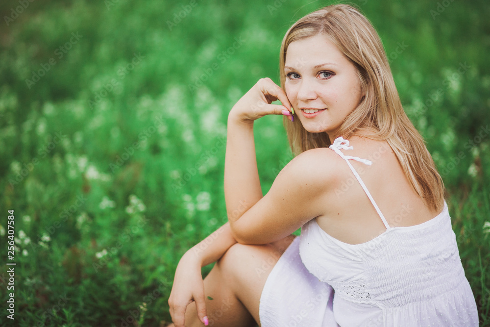 Portrait of beautiful smiling caucasian young girl sitting outdoors on green grass at summer meadow. Horizontal color photography. Portrait of beautiful smiling caucasian young girl sitting outdoors on green grass at summer meadow. Horizontal color photography.